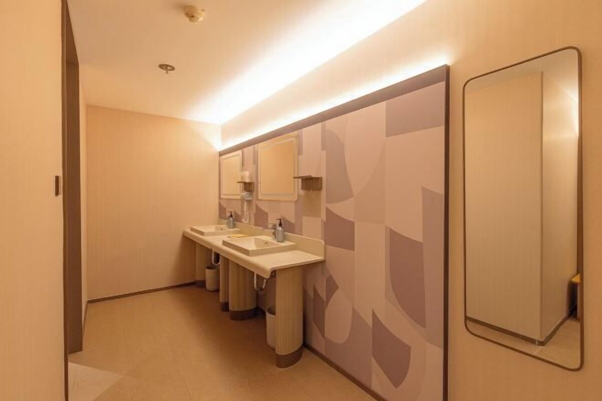 A modern bathroom with three sinks, a large mirror, and a geometric-patterned wall.