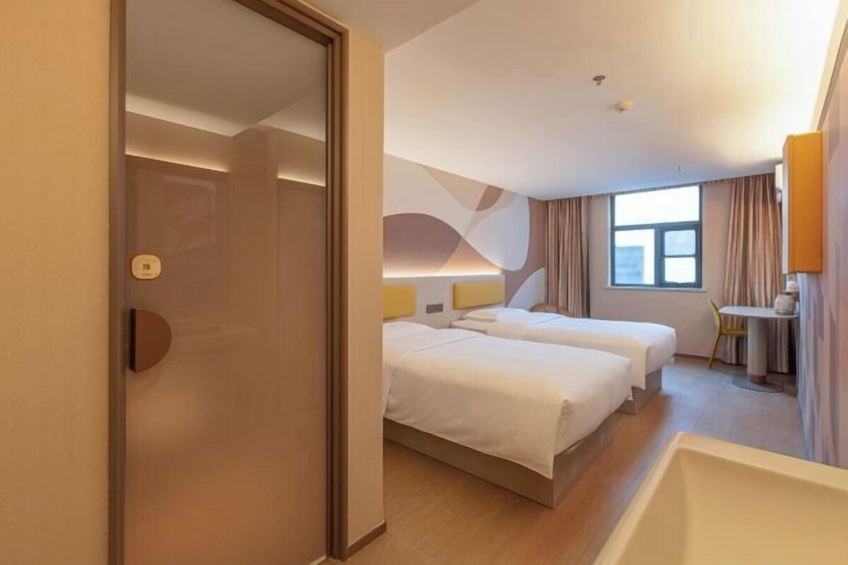 A hotel room with two beds, a desk, a chair, and a large window.