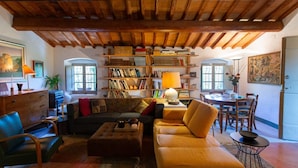 Una sala de estar acogedora con techo de madera, una estantería llena de libros, un sofá, una mesa de centro y un comedor con sillas y una mesa.