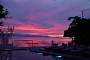 Zona de piscina con sillones de descanso y vista al mar durante el atardecer.