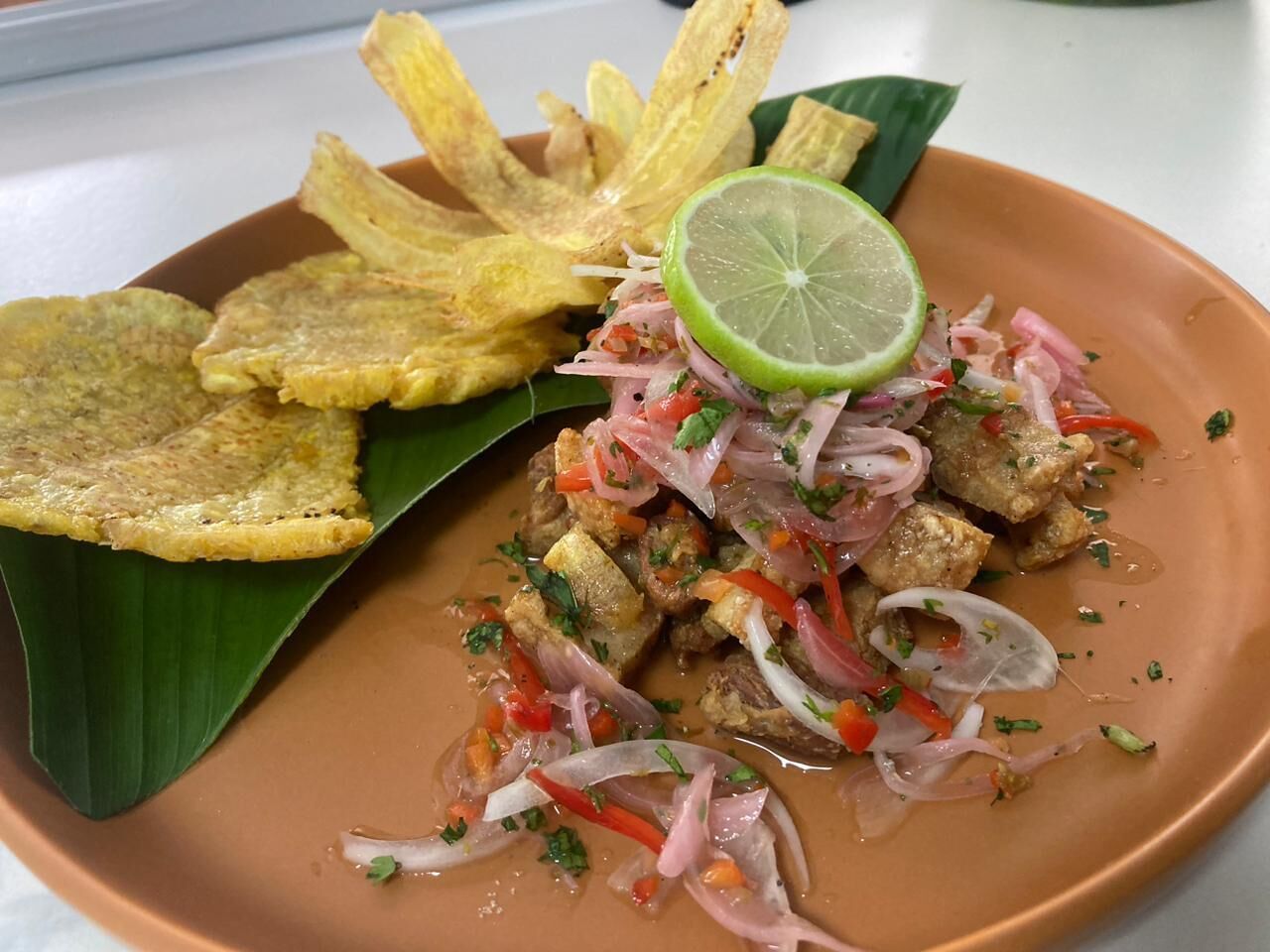 Prato de comida com bananas fritas, um pedaço de limão e salada com cebolas e ervas.