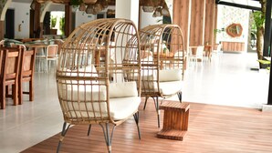 Wicker chairs with cushions on a wooden deck, a wooden table, and a modern interior with tables and chairs in the background. - Hotel Boutique Palma Arena (Turbo)