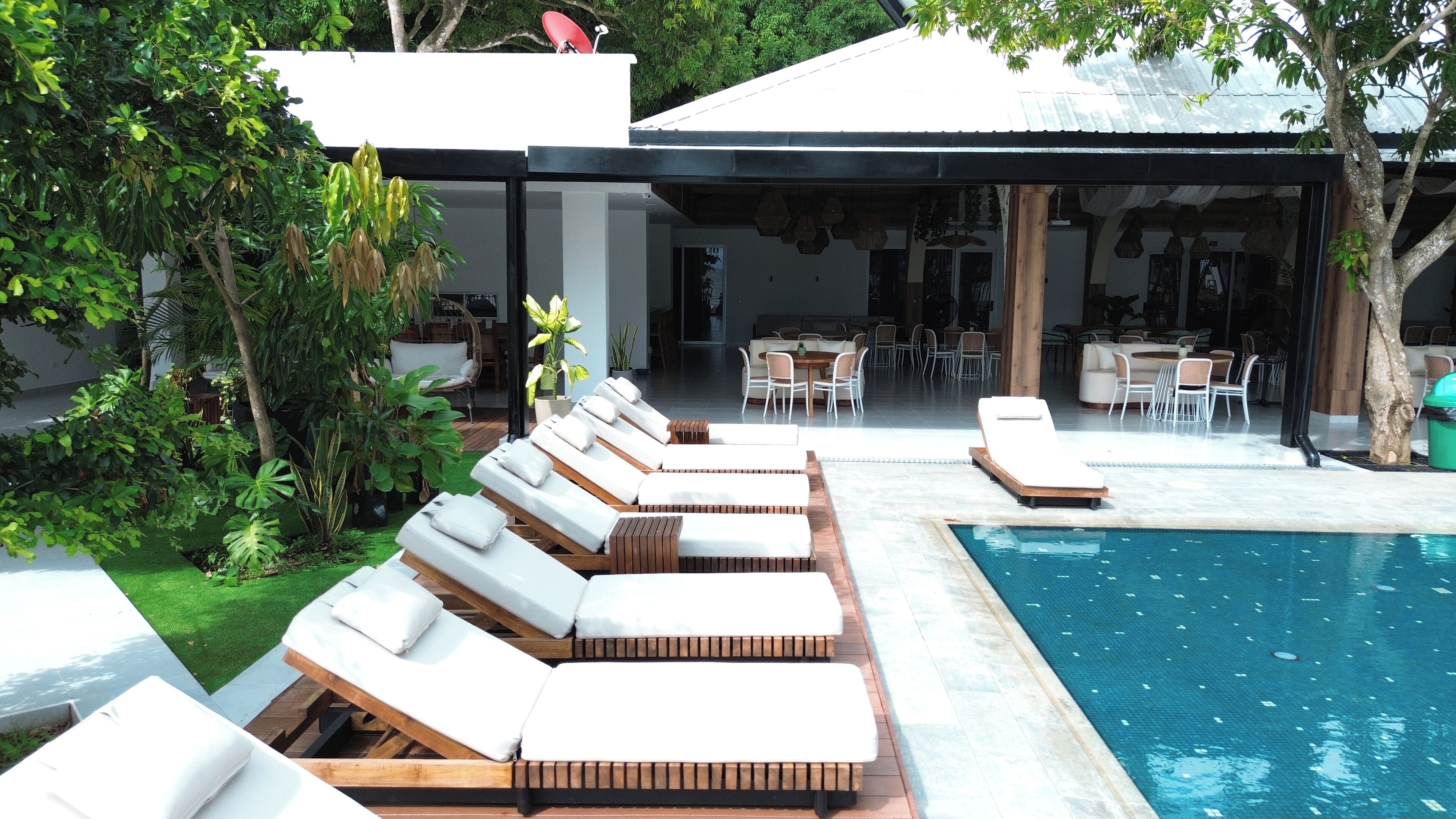 Zona de piscina con tumbonas y un área de comedor con mesas y sillas.