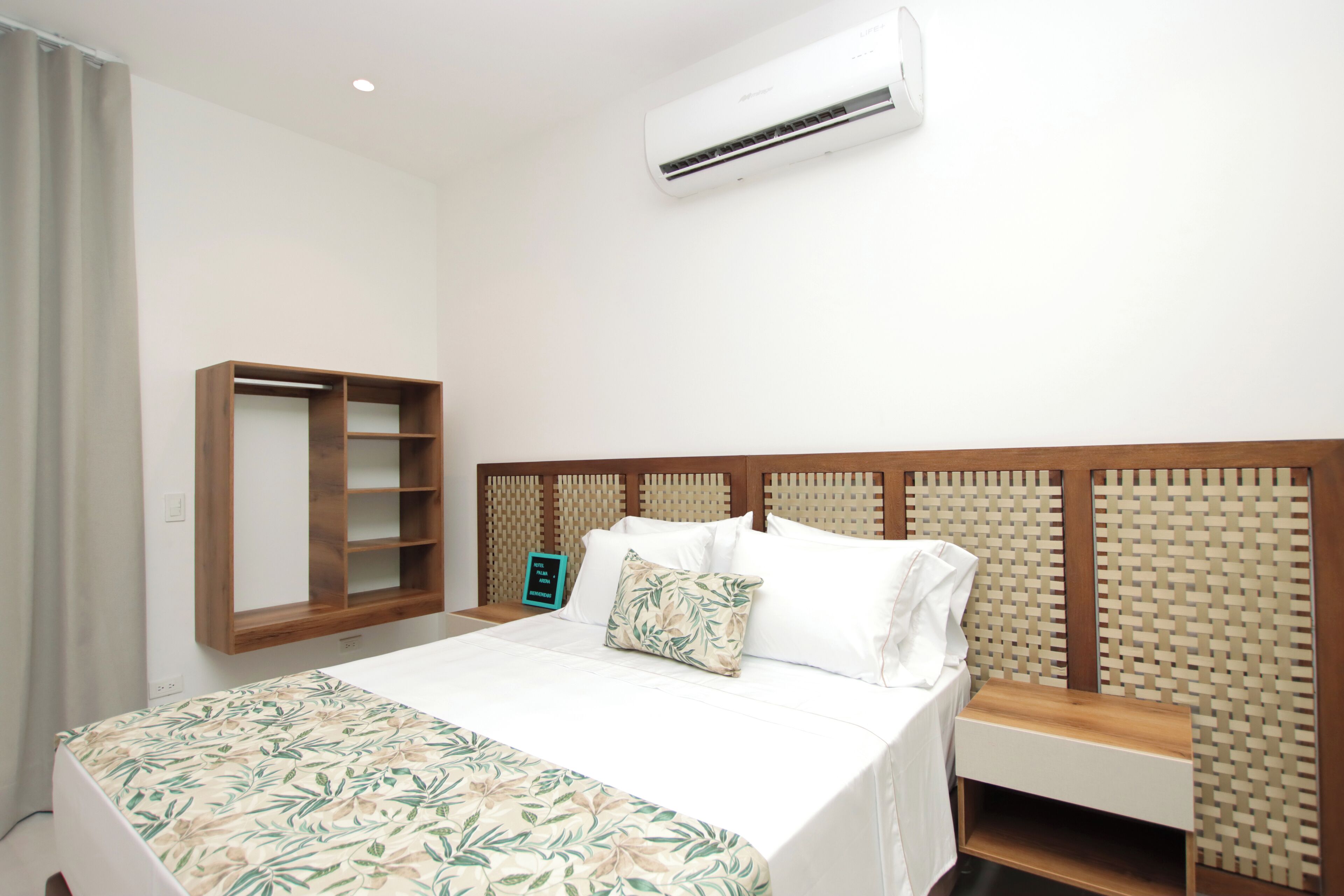 Una habitación de hotel con una cama, un armario de madera, una mesita de noche y un equipo de aire acondicionado.