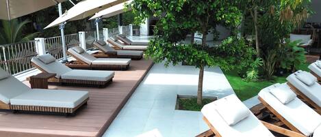 Un área de lounge en la azotea con múltiples tumbonas, una terraza de madera y un pequeño jardín con árboles y plantas.