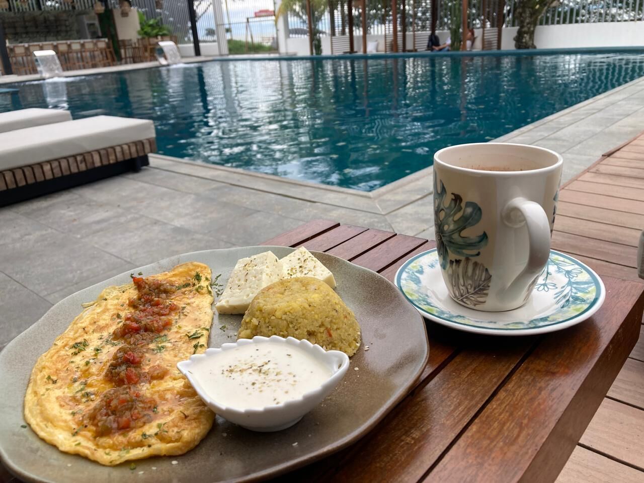 A dining table with a plate of food, a cup, and a pool in the background.