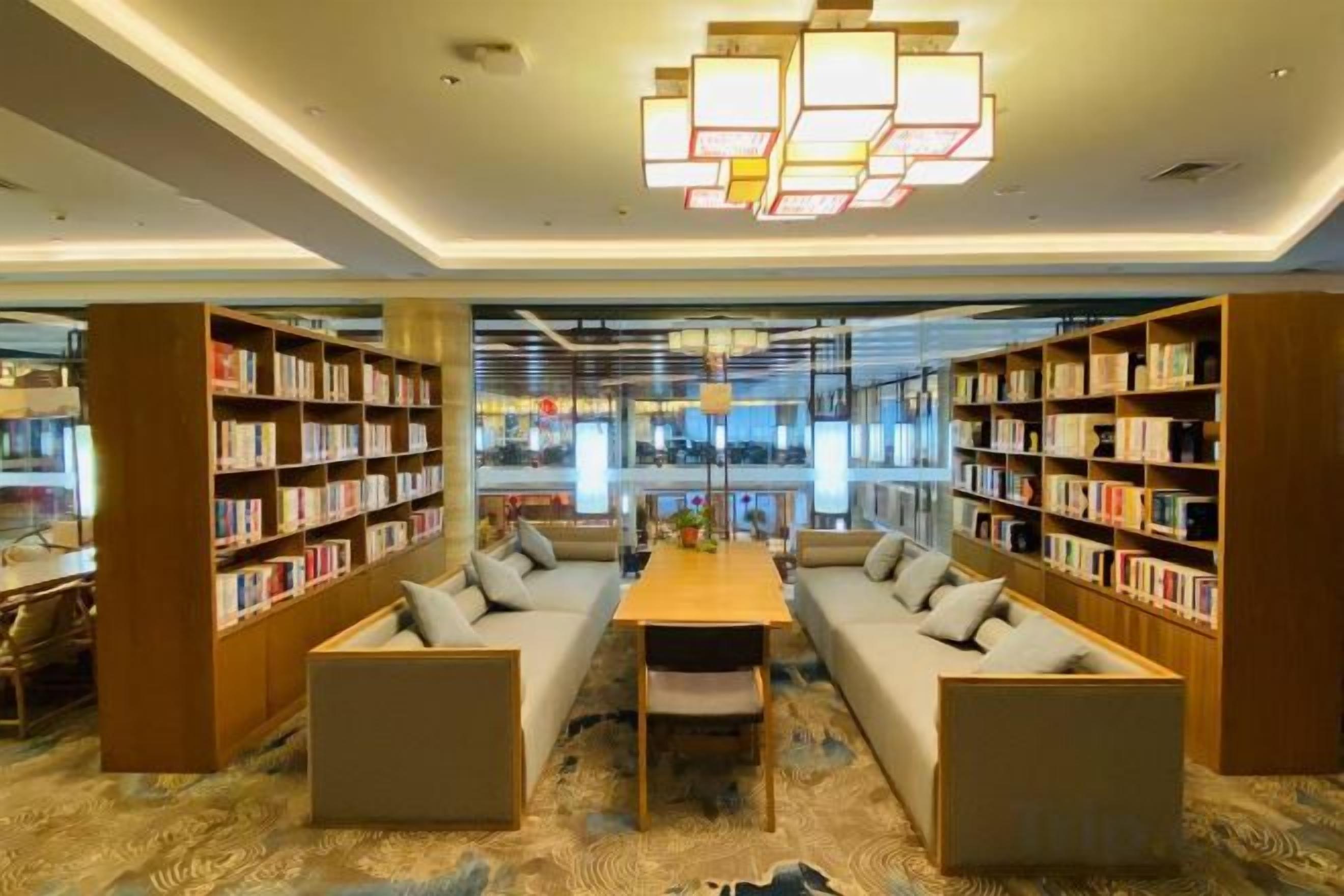 A modern library with bookshelves, seating areas, and a central table.