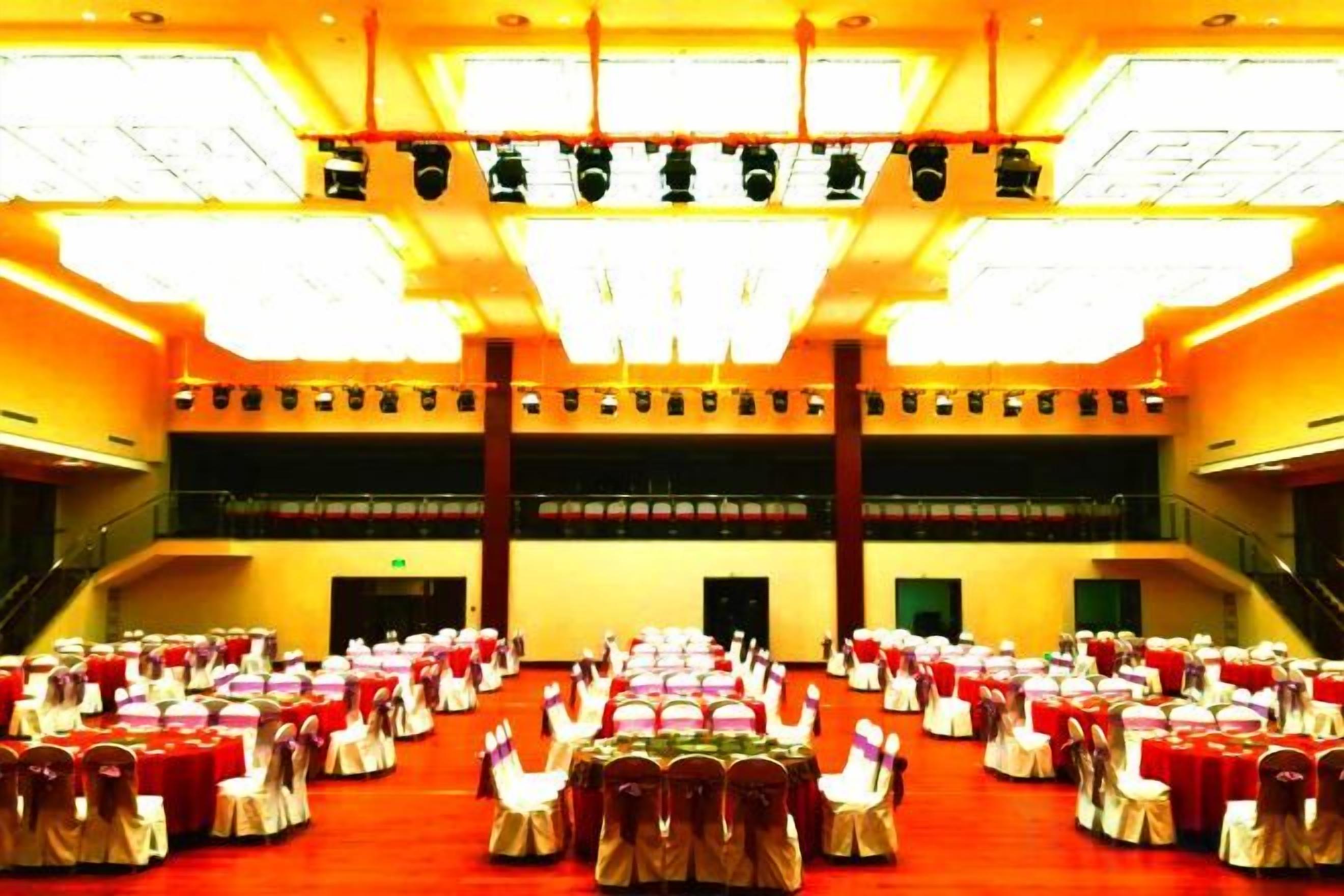 A large hall with rows of tables and chairs, a staircase, and a balcony.