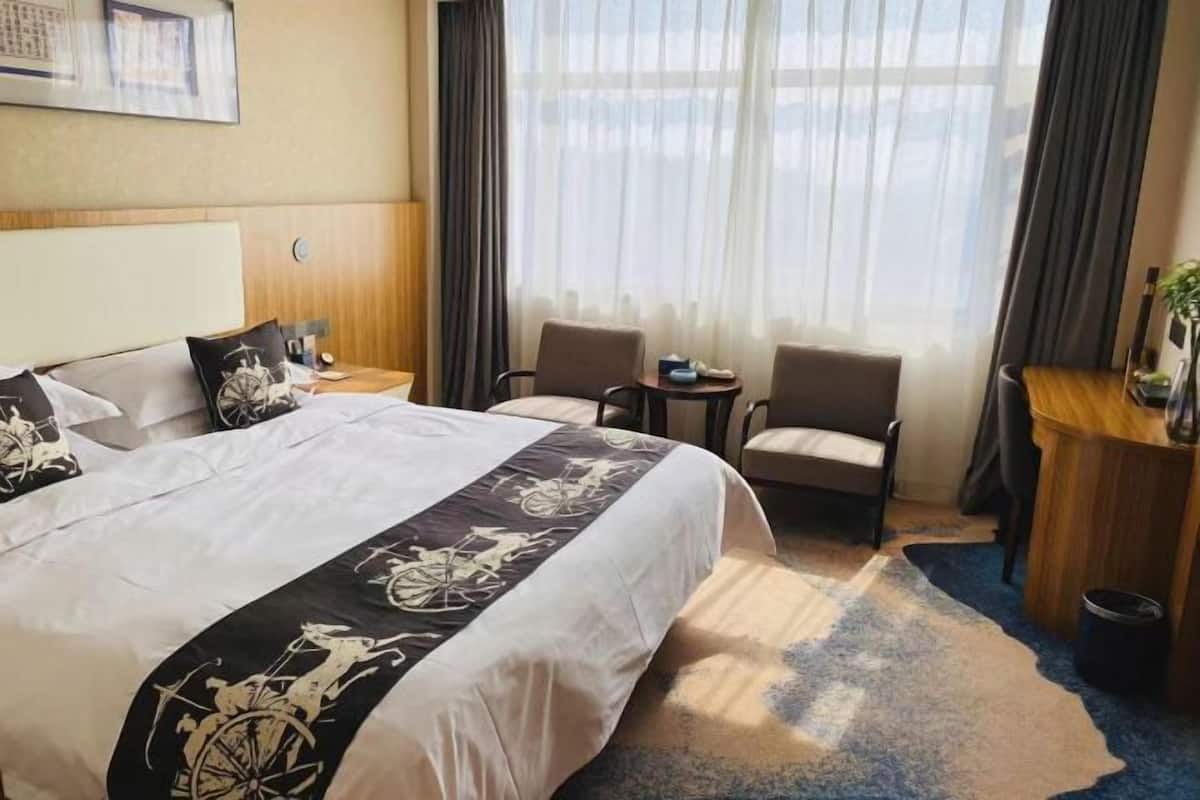A hotel room with a large bed, two armchairs, a small table, and a window with curtains.