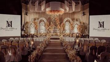 Un espacio interior con escenario, filas de sillas y decoración floral.