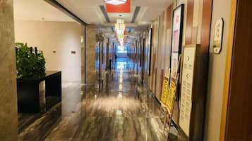 A hotel corridor with a shiny marble floor, a reception desk, and a signboard.