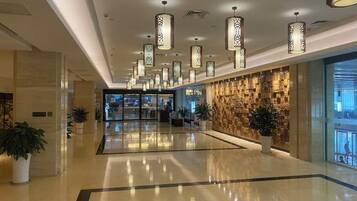 Un vestíbulo de hotel con piso pulido, lámparas colgantes, pared de piedra y plantas en macetas.