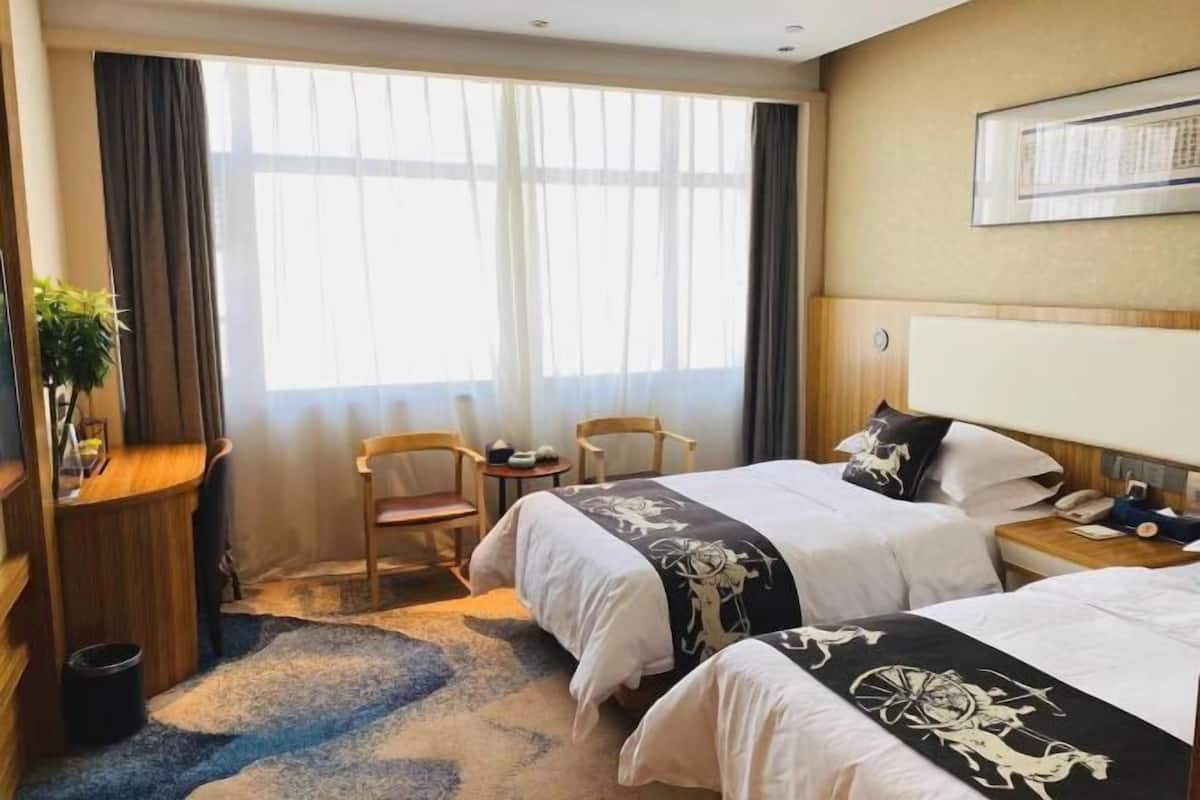 A hotel room with two beds, a desk, a chair, a small table, and a large window with curtains.