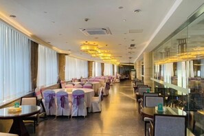 Un espace de restauration d’hôtel avec des tables et des chaises rondes, de grandes fenêtres et un design moderne au niveau du plafond.
