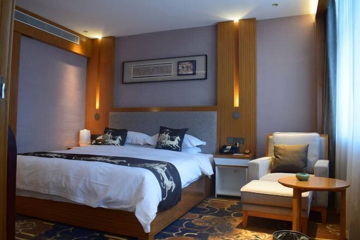 A hotel room with a bed, bedside table, chair, and a small table.