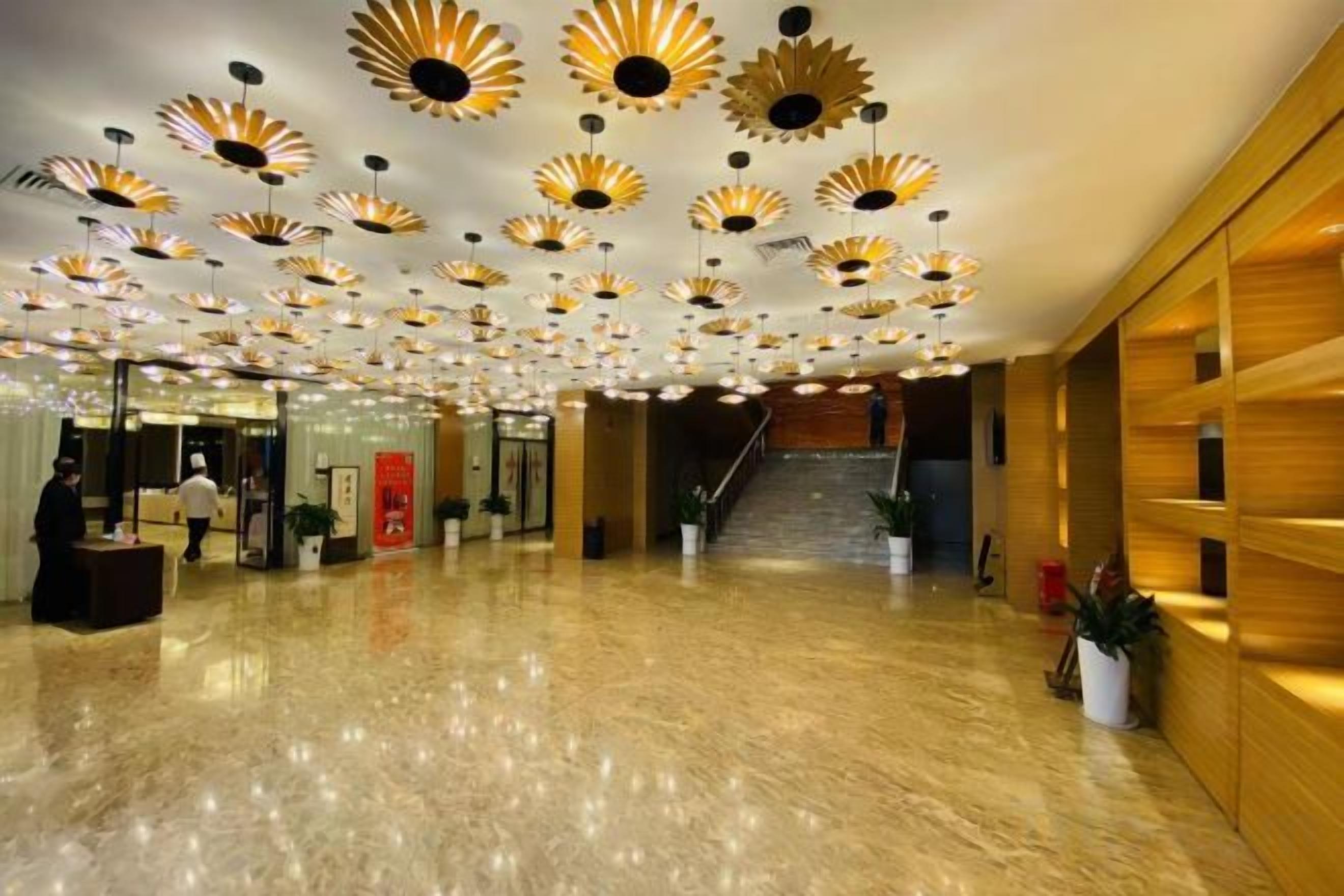 Vestíbulo de hotel con piso de mármol pulido, una escalera y un techo con lámparas decorativas.