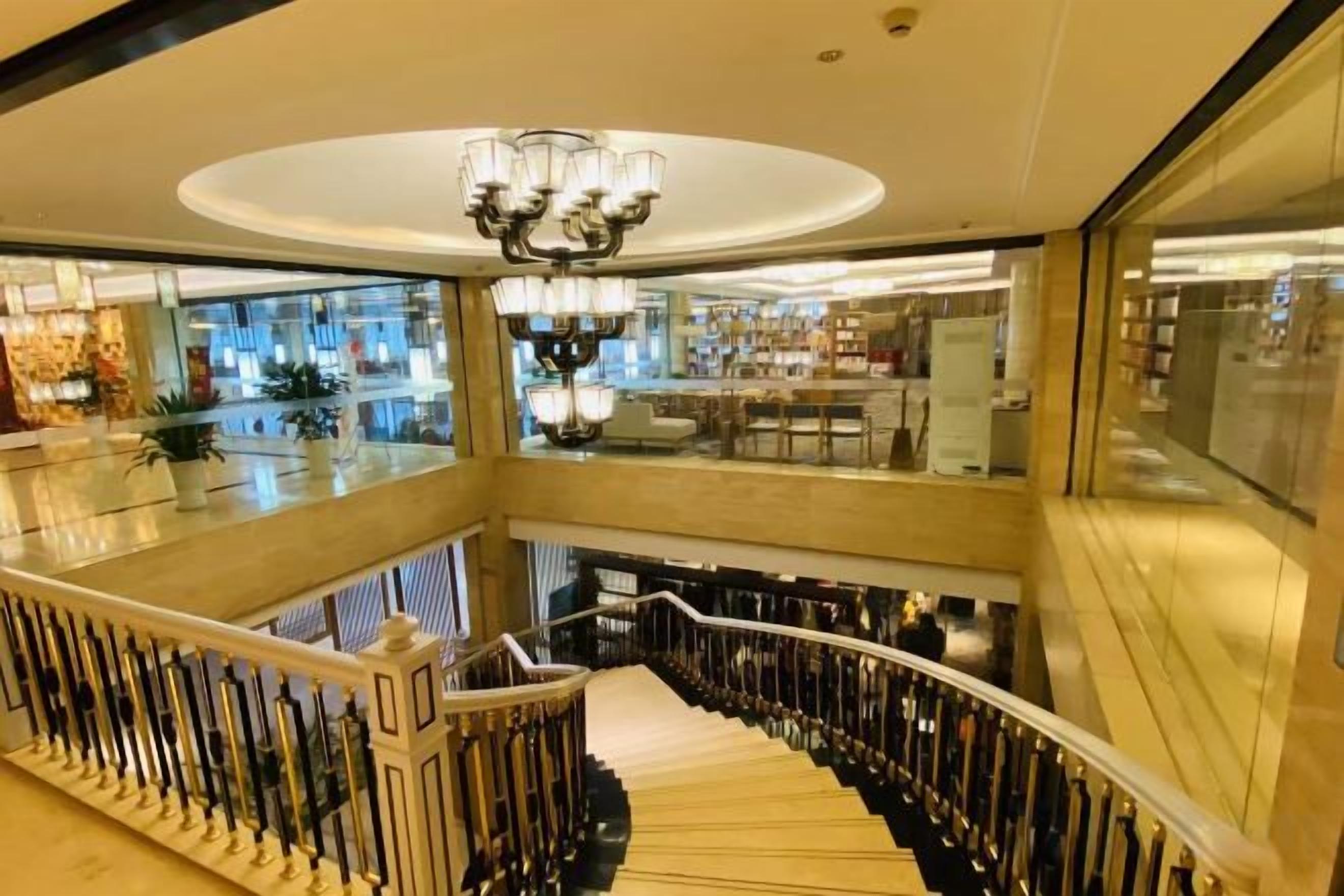 Un interior de varios niveles con una gran escalera, un candelabro y vistas al piso superior.