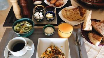 A breakfast setting with a plate of scrambled eggs, a bowl of sliced kiwi, a glass of orange juice, and a cup of black coffee.