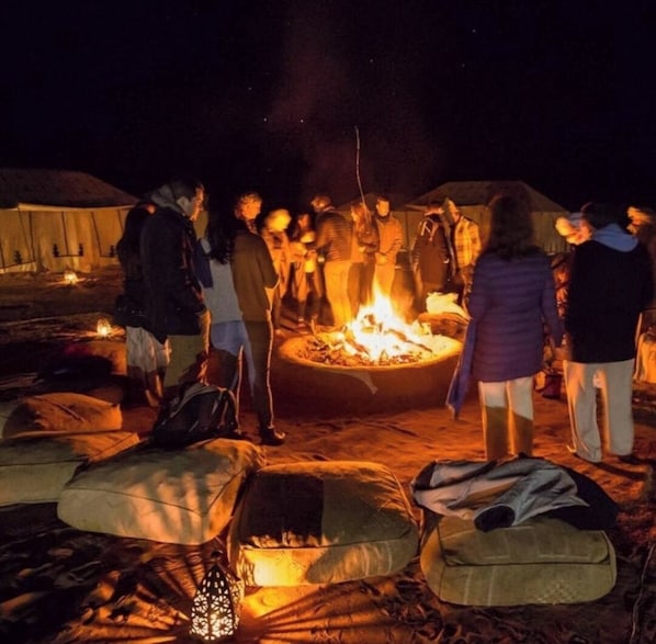 A group of people gathered around a campfire at night, with tents and sleeping bags in the foreground. - Desert Season Luxury Camp (Taouz)