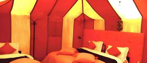 A tent-style room with two beds, each with orange bedding and white pillows.