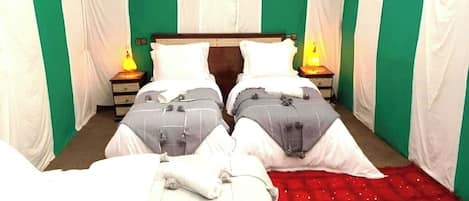 A room with two beds, each with a pillow and a nightstand with a lamp.