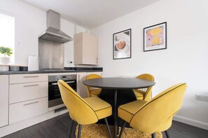Une cuisine moderne avec des meubles blancs, une hotte en acier inoxydable et une table ronde entourée de chaises jaunes.