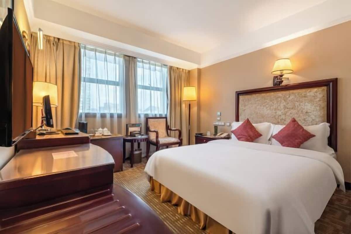 A hotel room with a large bed, a desk, a chair, and a lamp.