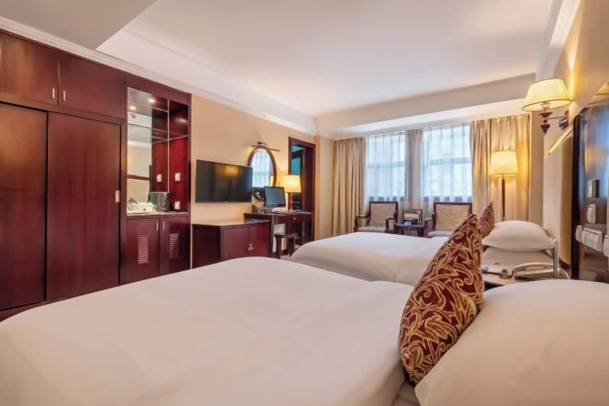 A hotel room with two beds, a desk with a chair, a TV, and a wardrobe.