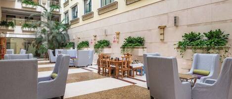 A hotel lobby with seating areas, a central table, and potted plants.