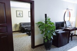 A hotel room with a dark wooden door, a black desk with a computer, a potted plant, a black leather sofa, and a patterned carpet. - Wuyue Hotel (Guiyang)