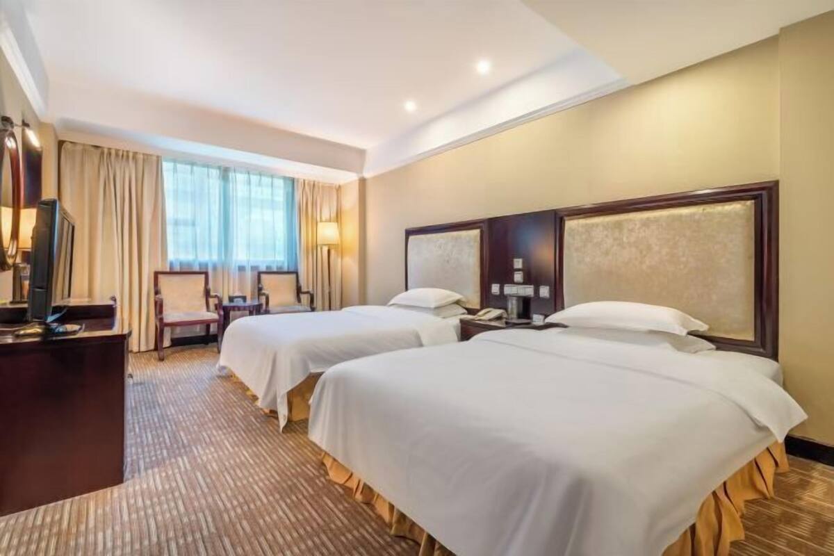 A hotel room with two beds, a desk, a chair, and a TV.