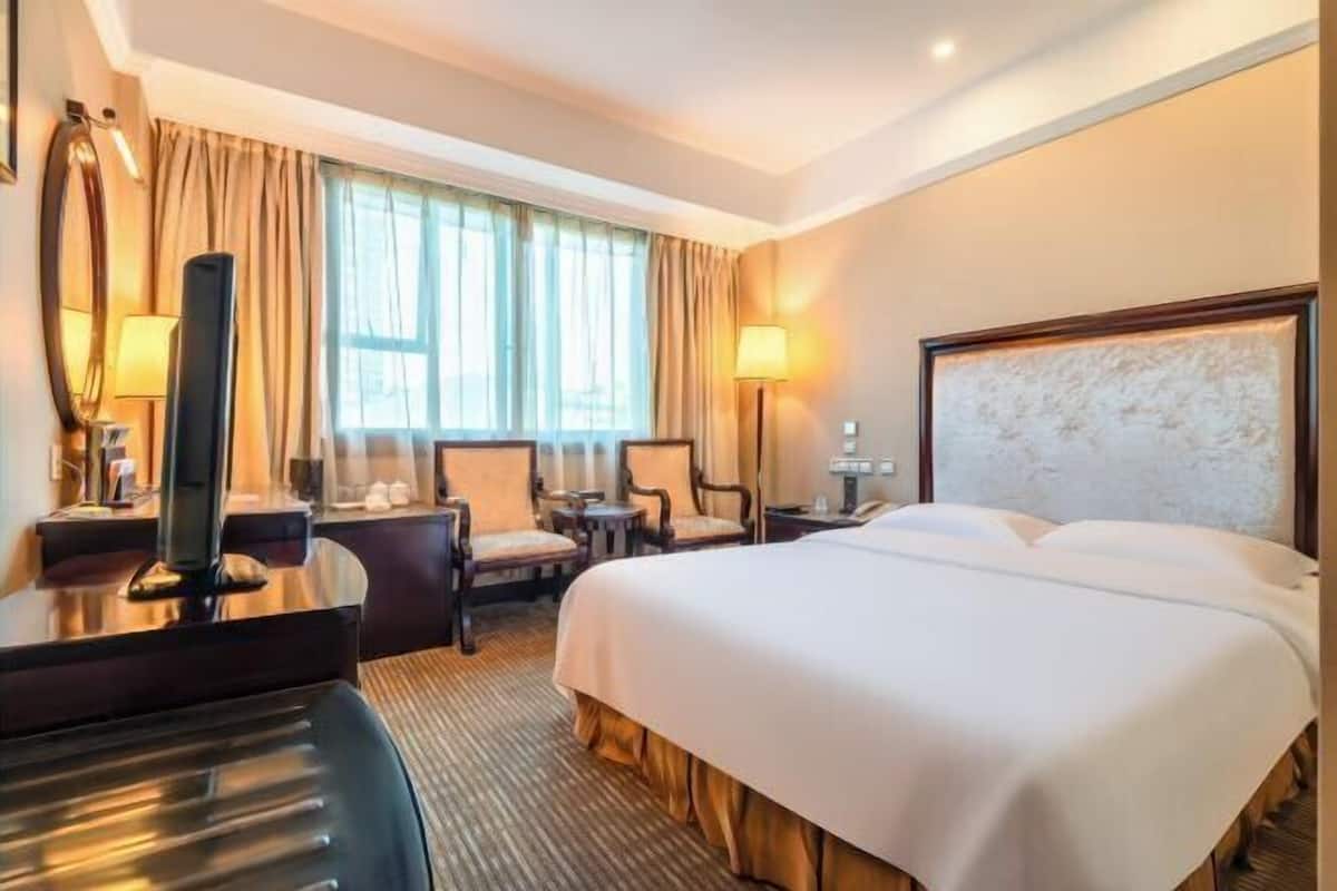 A hotel room with a large bed, two armchairs, a desk with a computer, and a TV.