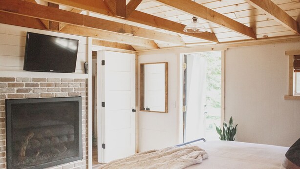 A bedroom with a brick fireplace, a television, a bed with a blanket, and a large window.