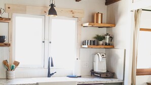A kitchen with wooden beams, a stainless steel dishwasher, a coffee maker, and a window above the sink.