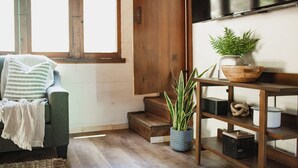 A cozy room with a green armchair, a wooden table with a plant, and a staircase leading to another level.