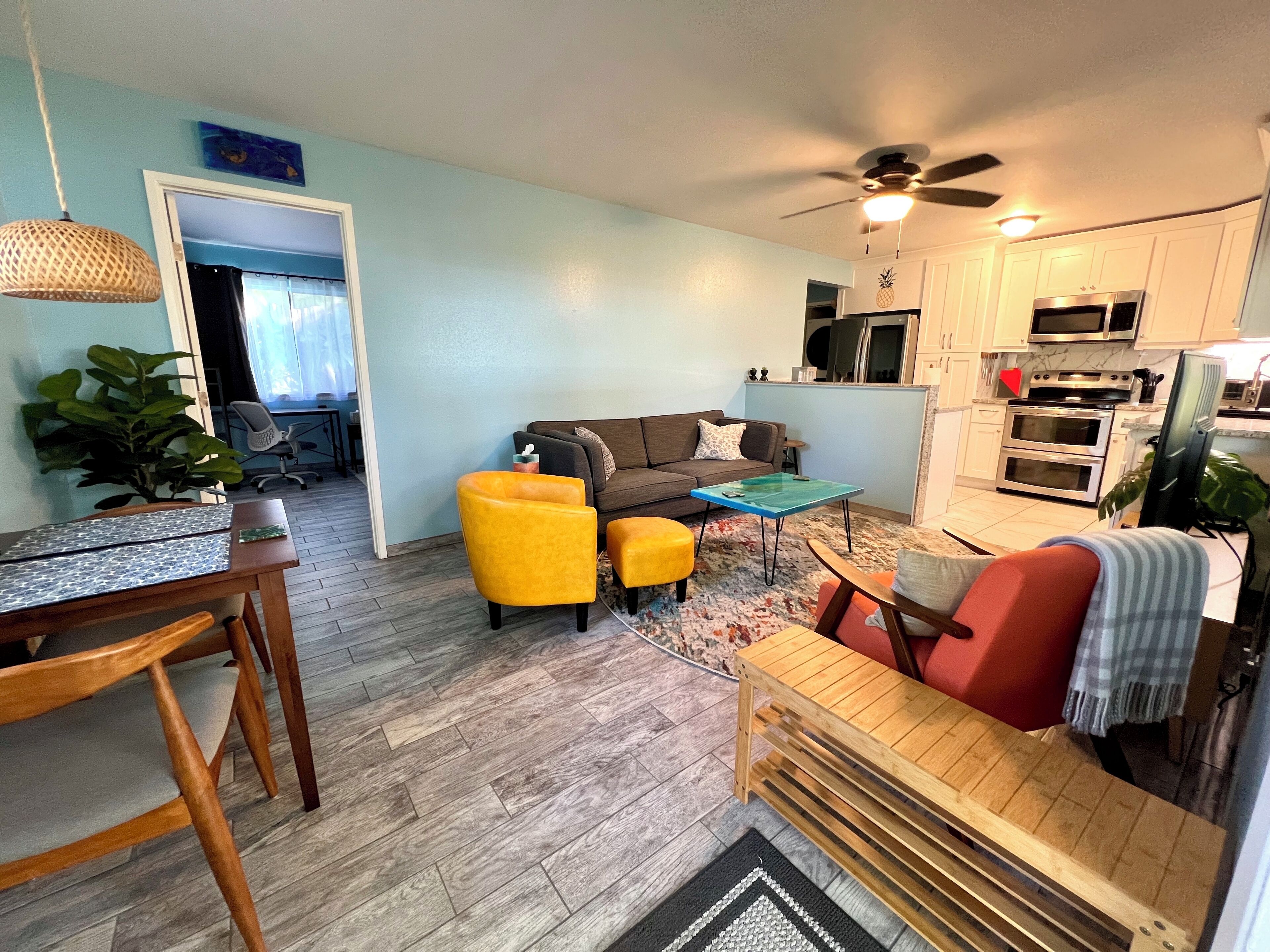 A compact living space with a dining area, a sofa set, a kitchen with modern appliances, and a ceiling fan.