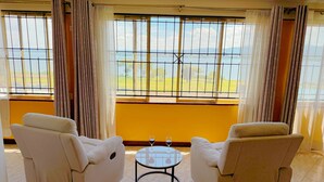 A room with two white armchairs, a small round table with a wine glass, and a large window with a view of a landscape.