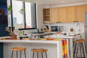 A modern kitchen with wooden cabinets, a central island with stools, and a view of the city. - Condesa 8th-floor 3BR for 10, AC and parking (Ciudad de México)