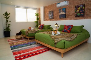 Ein Zimmer mit zwei grünen Betten, einem großen Fenster und einer Backsteinwand mit Kunstwerken.