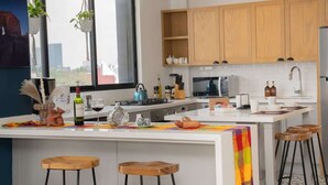 Une cuisine moderne avec des meubles en bois, un îlot central doté de tabourets et une vue sur la ville grâce à de grandes fenêtres.