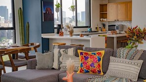 Un salon moderne avec un canapé gris, des coussins colorés et un coin repas comprenant des chaises et une table en bois.