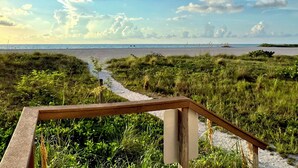 Un sentier menant à une plage, avec une rambarde en bois au premier plan.