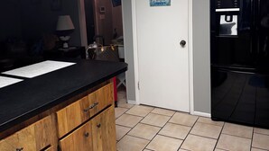 Una cocina con armarios de madera, encimera negra, dispensador de agua y una puerta con una pintura de atardecer.