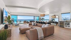 A spacious living area with a large brown sectional sofa, a dining table, and a kitchen area with wine storage. - Beachfront Boho Dream Penthouse. Walk 2 Everything!   Newly designed  SLEEPS 10! (Oceanside)