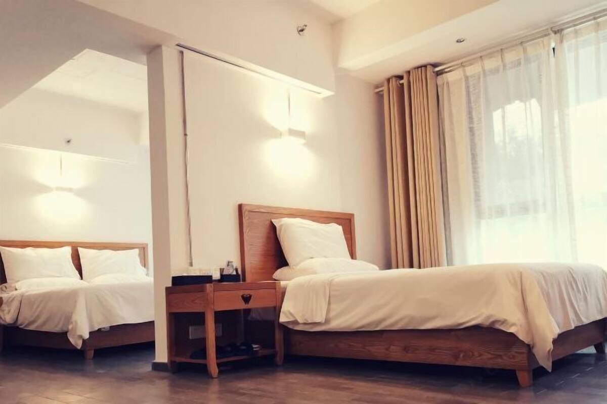 Ein Hotelzimmer mit zwei Betten, einem Nachttisch, einem Spiegel und einem Fenster mit Vorhängen.
