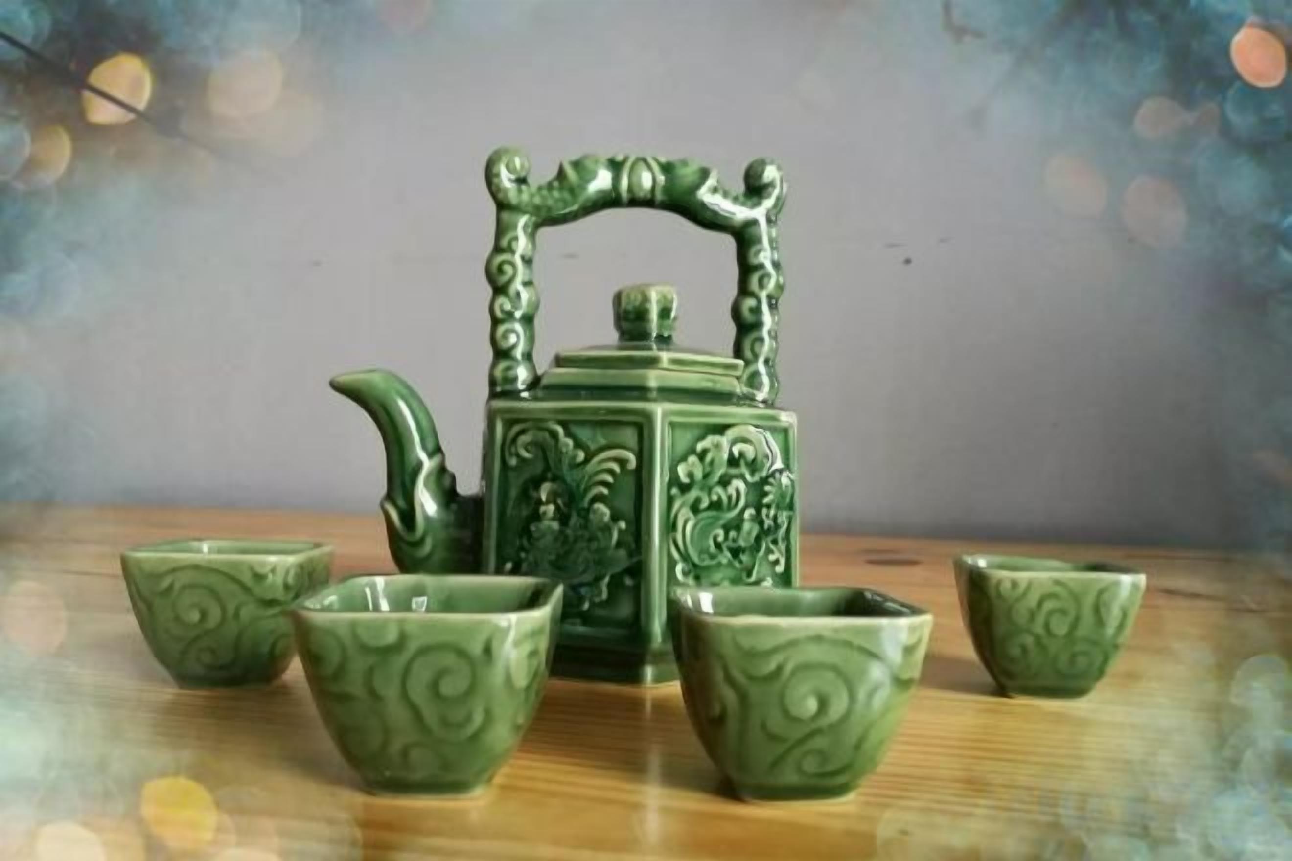 A set of green ceramic tea set with a teapot and four cups on a wooden surface.