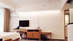 Een moderne hotelkamer met een bed, een houten bureau en een flatscreen televisie bevestigd aan een witte bakstenen muur.