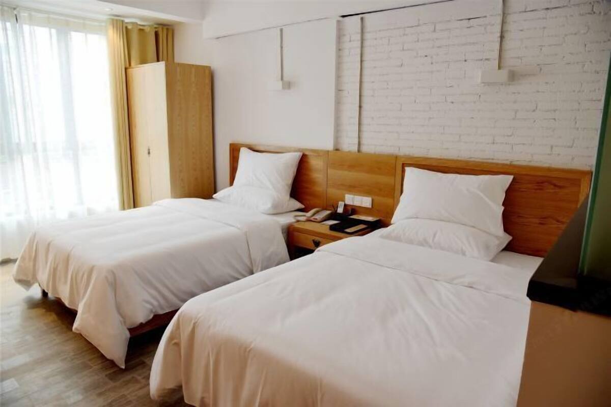 Ein Hotelzimmer mit zwei Betten, einem Holzschrank, einer Ziegelwand und einem Fenster mit Vorhängen.