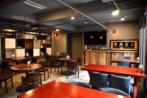A restaurant with round tables, rectangular tables, and booths. There are chairs around the tables, and a television is mounted on the wall.