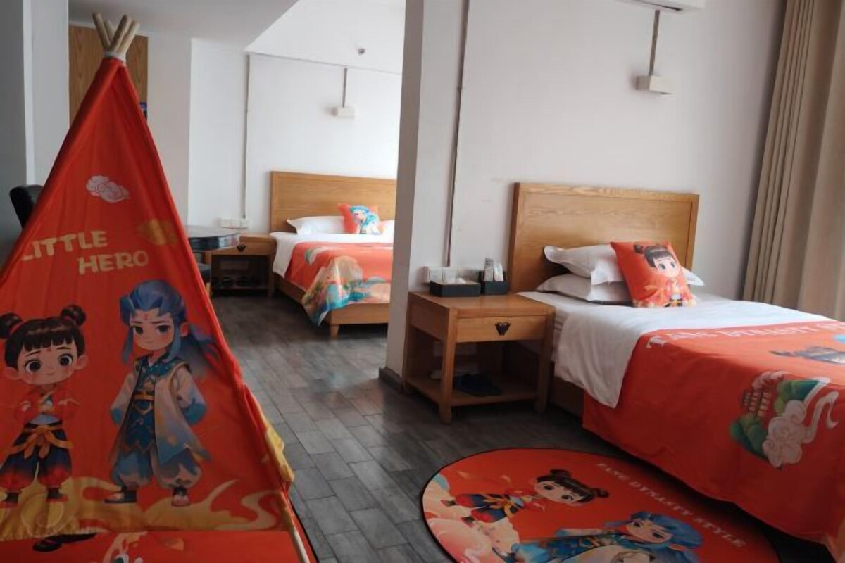 Une chambre d’hôtel avec deux lits, une table de chevet, une lampe et une tente rouge ornée de personnages de dessins animés.